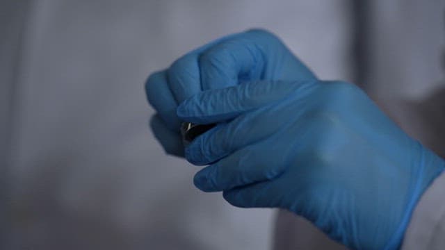 Gloved hands handling a small object in a laboratory