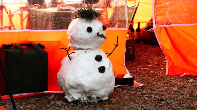 Snowman made with pin cones and pine branchses next to an orange tent