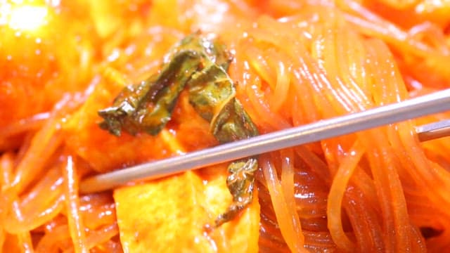 Chopsticks holding glass noodles of spicy tteokbokki