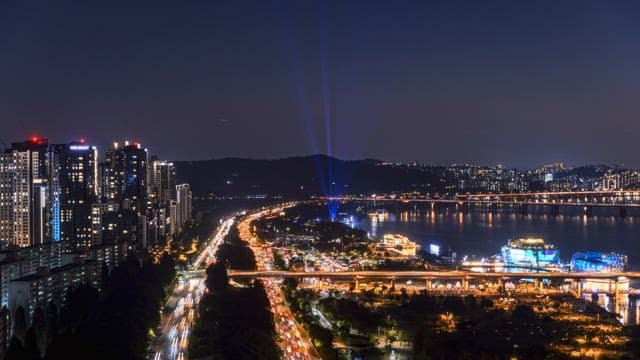 Night view of a vibrant city with lit road and illuminated buildings along a river