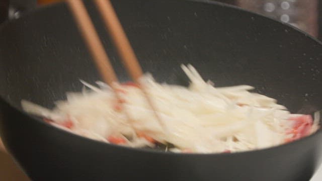 Frying shredded potato and meat in a wok with chopsticks