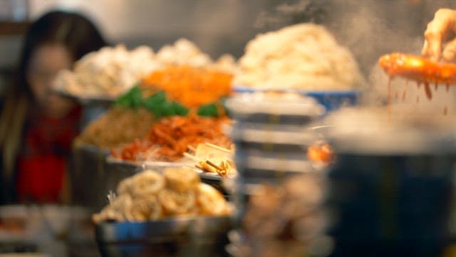 Gwangjang market street vendor serving tteokbokki with a ladle