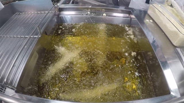 Putting skewered sand eels into a deep fryer full of oil in a commercial kitchen