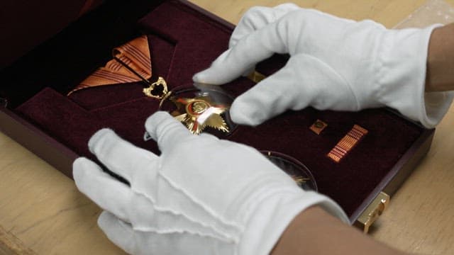 Gloved hands arranging medals inside a velvet box