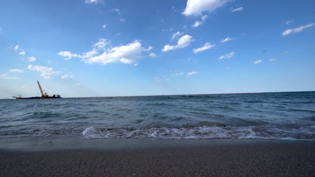 Waves lapping the shore with a distant construction crane in the background