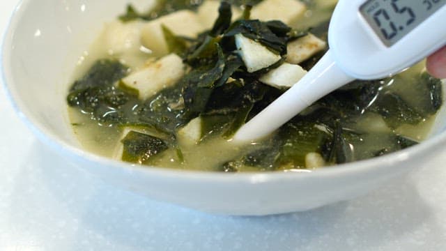 Hands testing seaweed soup salinity with a salinity meter indoors