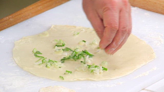 Scallions being spread on flour dough