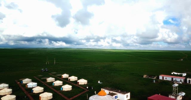 Vast grassland with yurts and cloudy sky