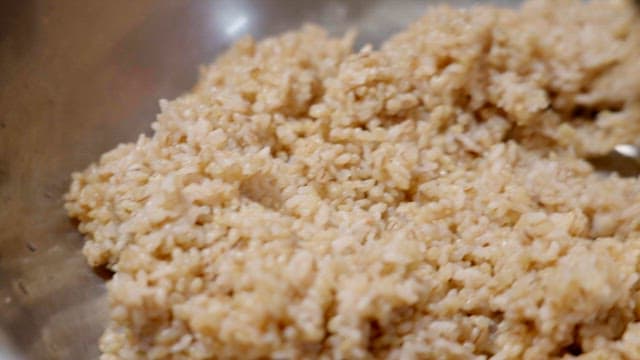 Stirring freshly cooked brown rice in a bowl with a wooden spatula