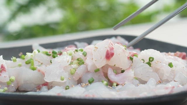 Fresh raw fish topped with green onions and sesame seeds, dipped in sauce