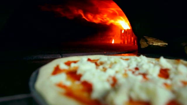 Pizza being baked in a wood-fired oven with intense flames