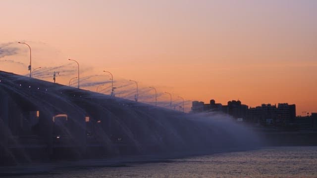 Bridge with water fountains at sunset in the city