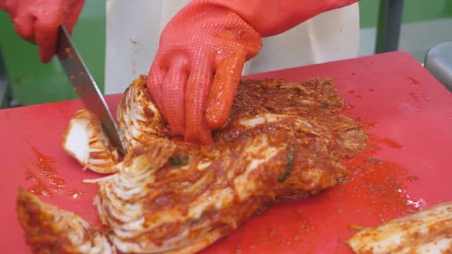 Person preparing kimchi on a red cutting board