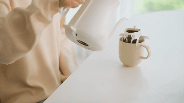 Woman pouring water into cup with coffee pot on table