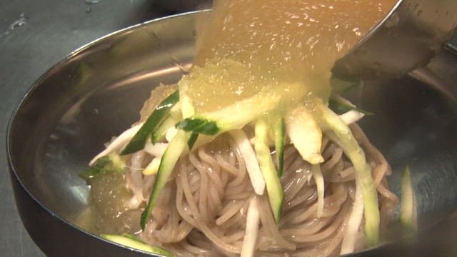 Preparing cold noodles by adding spicy sauce and pouring broth