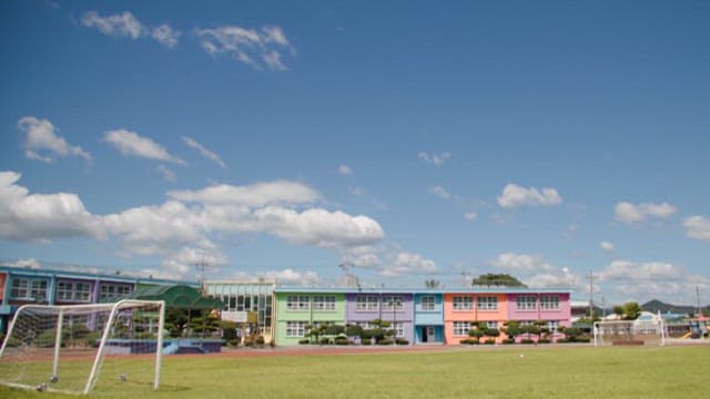 Colorful elementary school buildings and playground under a sunny sky with drifting clouds