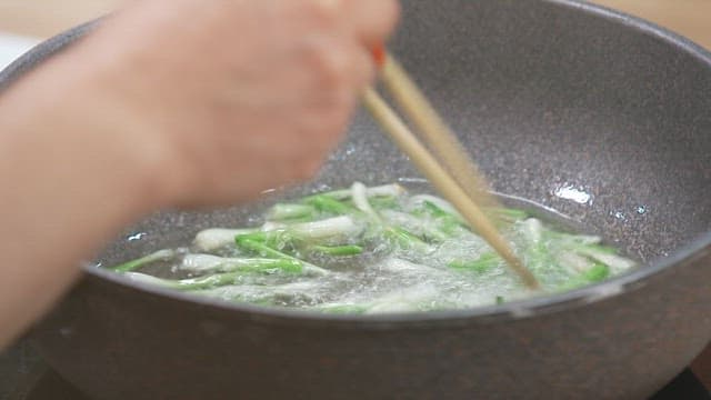 Cooking fresh green onions in boiling water in a frying pan