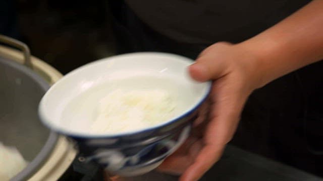 Hand scooping steamed rice into a bowl indoors