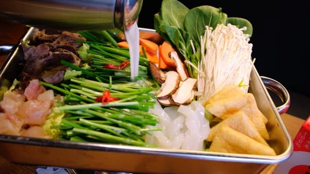 Broth for hotpot poured over fresh vegetables and meat prepared in a pot