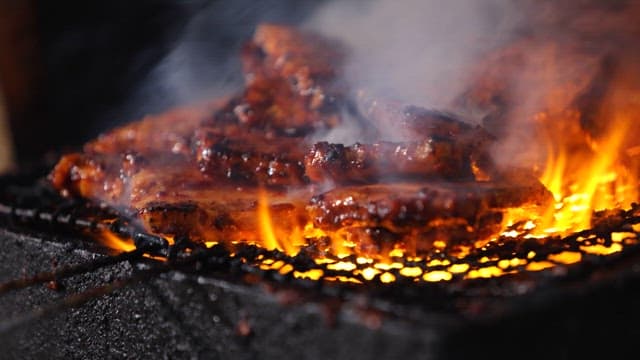 Spicy grilled pork belly sizzling on a grill over blazing charcoal