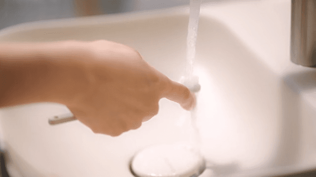 Washing a toothbrush under running water from a sink faucet