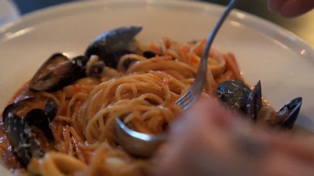 Person enjoying seafood pasta at restaurant