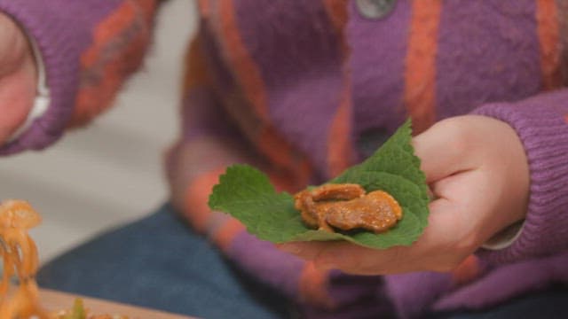 Hands placing stir-fried spicy pork on perilla leaves with chopsticks