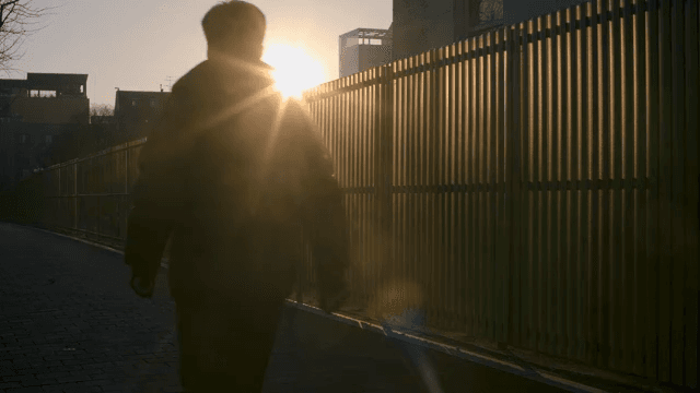 Man Walking by a Fence around the Buildings at Sunset