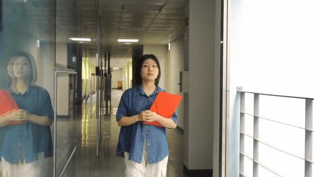 Woman walking down a hallway holding a red folder