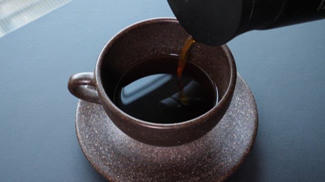 Pouring hot coffee into a brown cup
