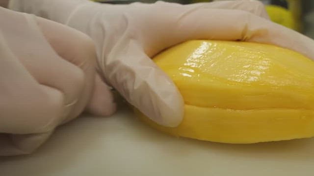 Hands slicing ripe yellow mango on white cutting board.