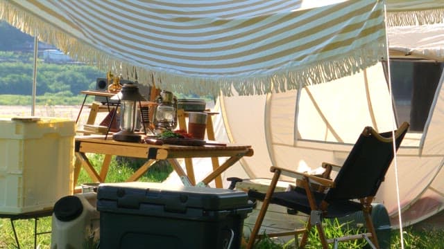 Outdoor campsite setup with tent and supplies under a striped canopy