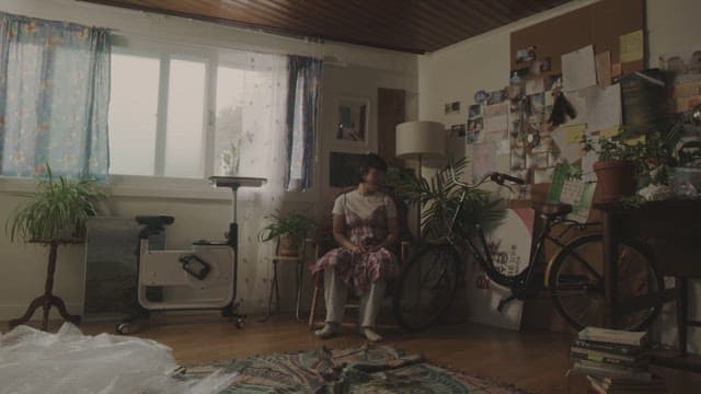 Woman sitting in a cozy room filled with plants and books.