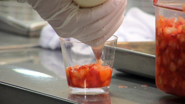 Whipped cream being added to a fruit cup