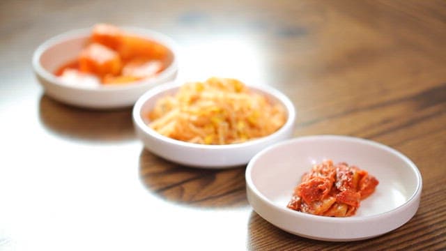 Plates of side dishes including kimchi and bean sprout salad on a wooden table