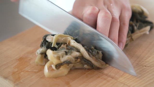 Cutting boiled dried radish greens with a knife on a cutting board