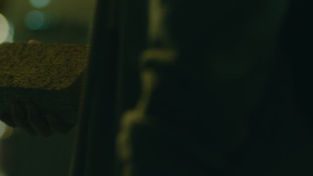Mysterious man holding a brick in his hand on a street at night