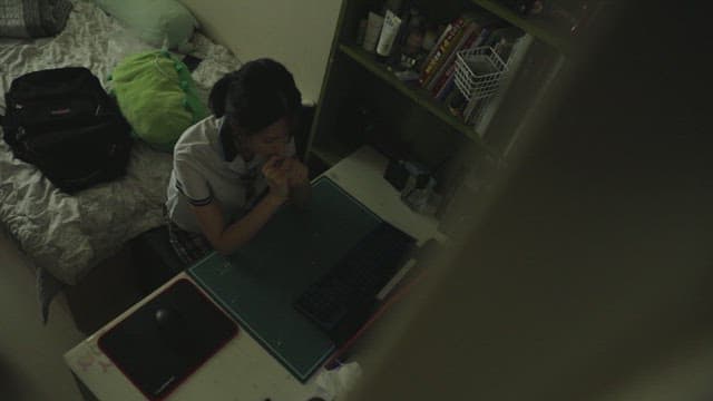Student lost in thought at desk in dark bedroom