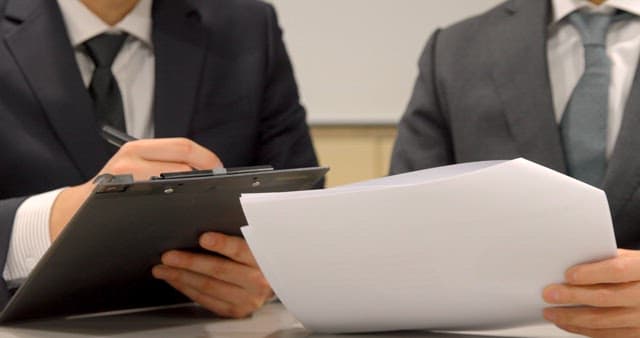 Businessmen Cross-Checking Documents at Desk