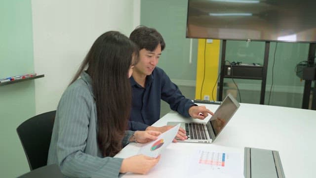 Two people discussing while looking at laptop in office