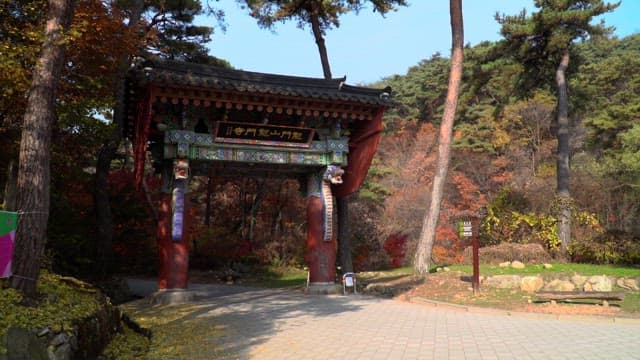 Tourists walking through a traditional wooden gate in a forest park during autumn.