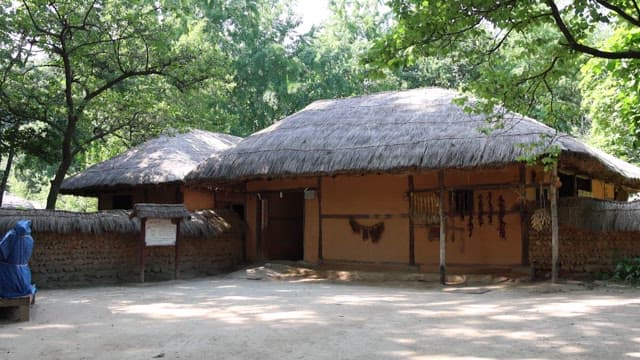 Traditional Korean house in a serene forest with informational signs outside.