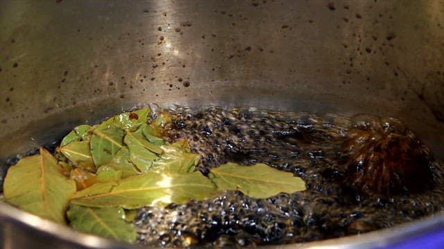 Black sauce with bay leaves boiling in a sot