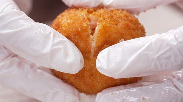 Gloved hand showing the inside of freshly fried crab meat fritters