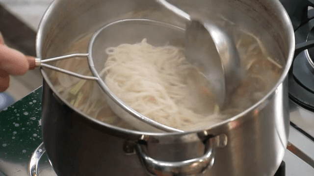 Noodles taken from hot broth are strained through a sieve and placed in a bowl