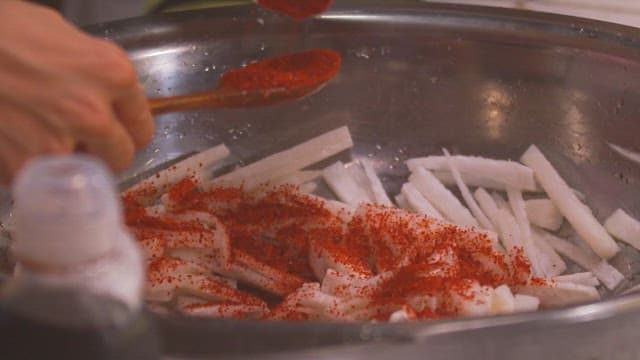 Make the julienne Korean radish salad by mixing the red pepper powder in a large bowl