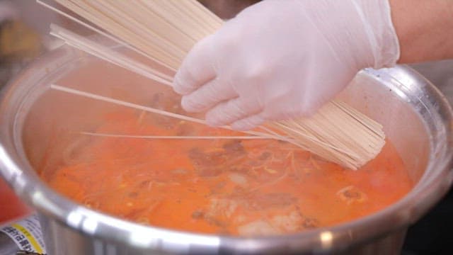 Noodles added to the spicy stew boiling in a pot