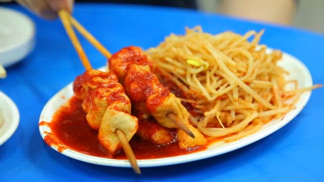 Chopsticks holding spicy fish cake skewers and bean sprouts