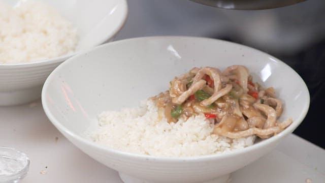 Stir-fried meat and vegetables served over rice in a white bowl