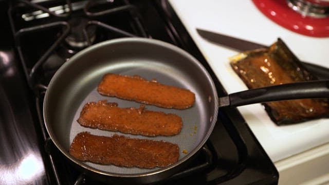 A person preparing a burger patty on a preheated oiled pan indoors